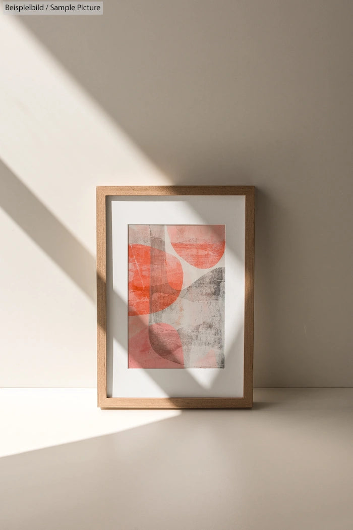 Framed abstract art with red circles and textured gray background, placed on a sunlit surface.