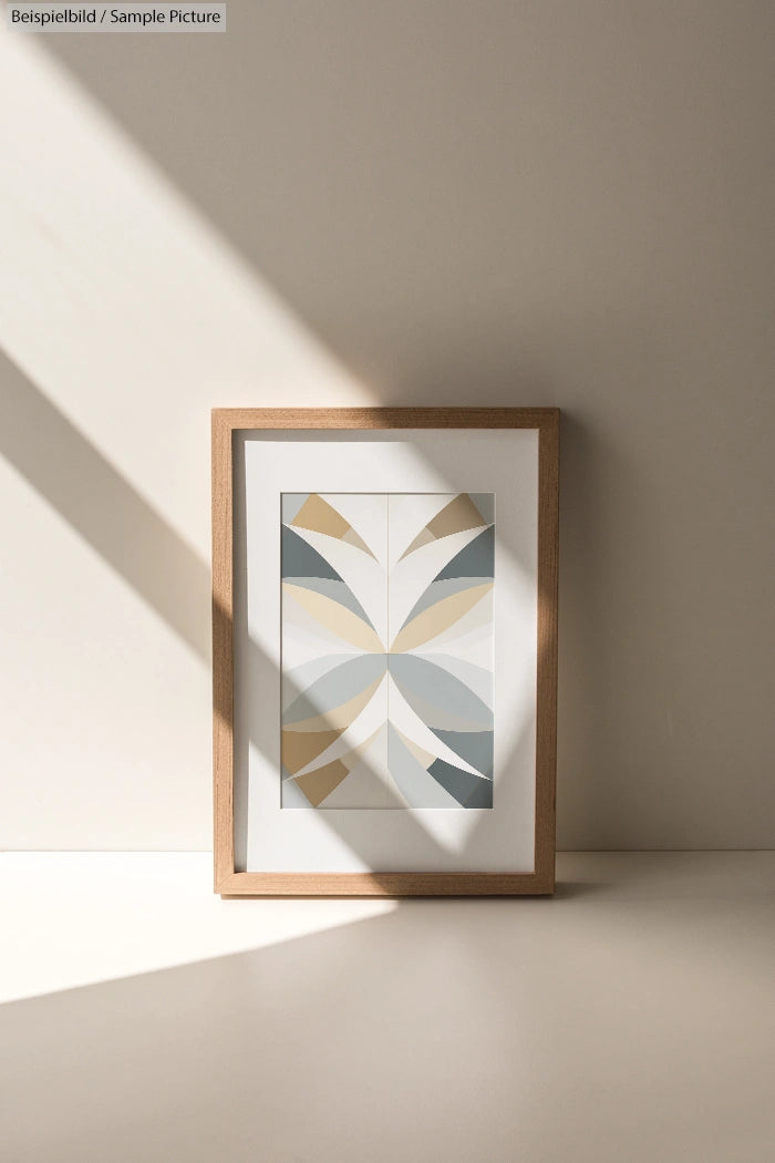 Framed abstract art with geometric shapes in muted tones leaning against a sunny wall.