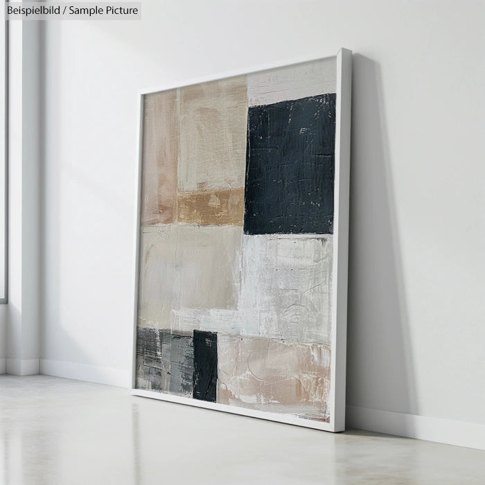 Framed abstract painting with black, white, and beige geometric blocks leaning against a white wall.