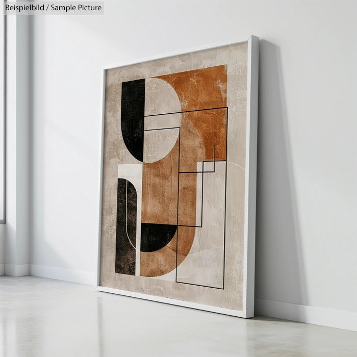 Framed abstract art with geometric shapes in brown, black, and beige tones leaning against a white wall.