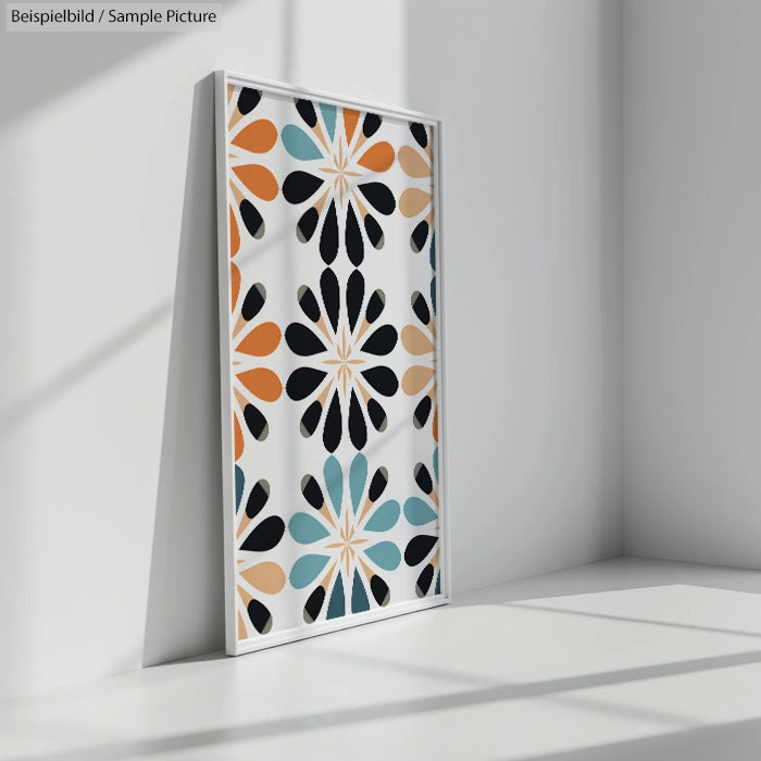 Abstract geometric artwork with orange, black, and teal leaf shapes in a framed picture leaning against a wall.