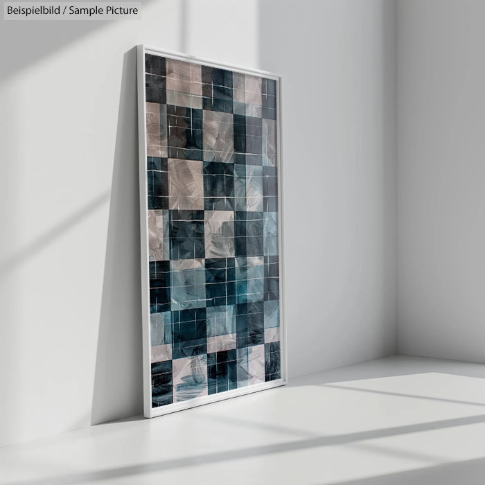 Framed abstract mosaic artwork with blue and gray tones leaning against a white wall.