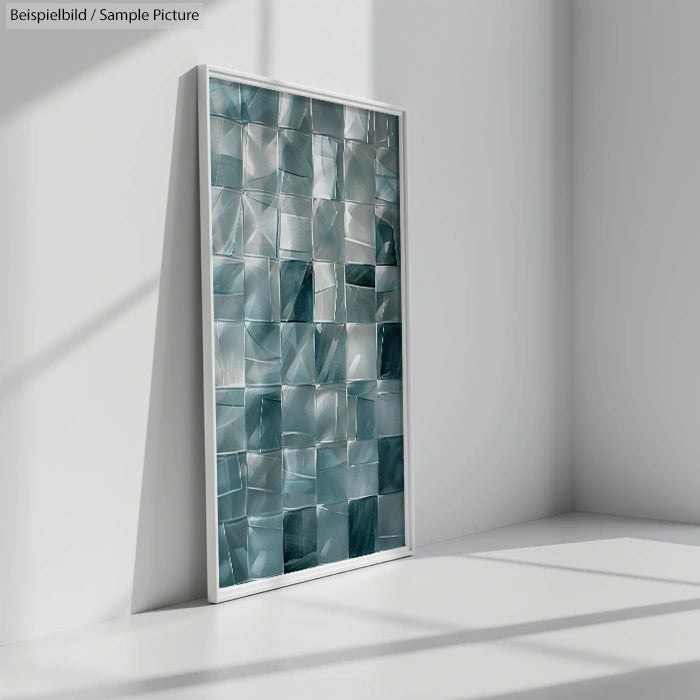 Framed abstract artwork with green and silver geometric pattern leaning against white wall in sunlit room.