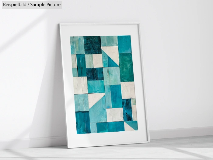 Framed abstract artwork with blue, teal, and white geometric shapes leaning against a white wall.