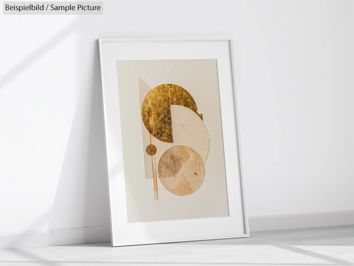 Framed abstract art print with geometric shapes in gold and beige tones, leaning against a white wall.