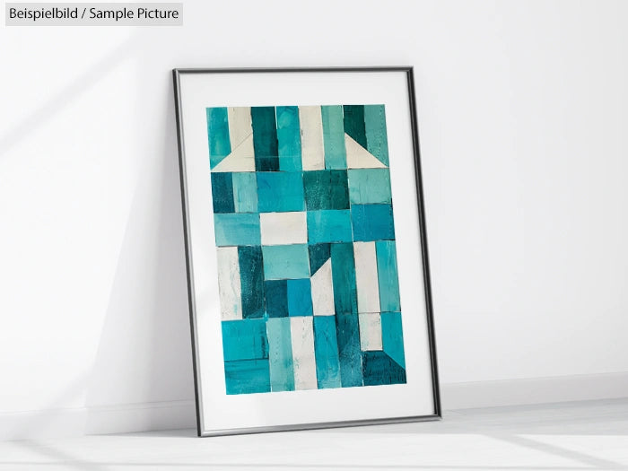 Framed abstract artwork with geometric blue and teal patterns leaning against a white wall.