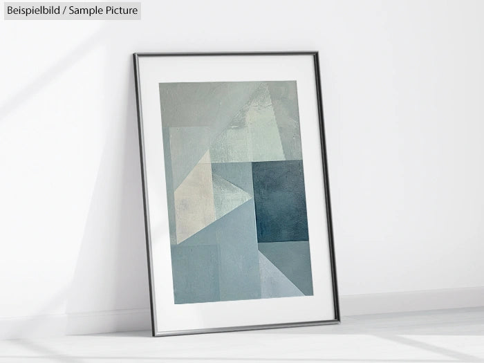 Framed abstract painting with geometric shapes in blue and gray tones, leaning against a white wall.