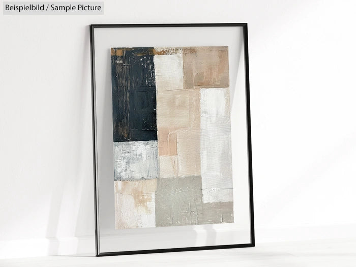 Framed abstract painting with beige, black, and gray geometric blocks on a white wall.