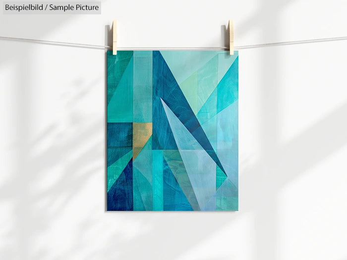 Geometric abstract painting with blue, teal, and turquoise shapes on a white background, hanging on a line with clips.