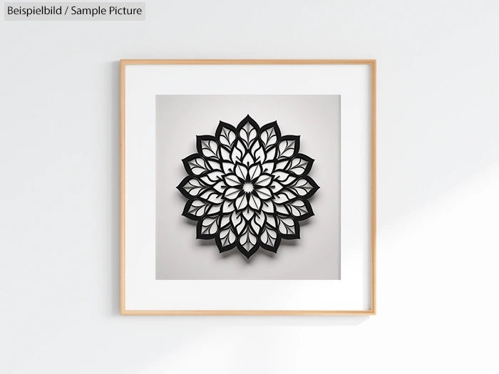 Black and white mandala art framed in light wood against a plain white wall.