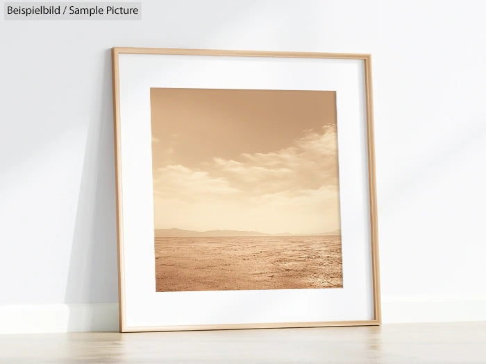 Framed sepia photograph of a desert landscape with cloudy sky, leaning against a white wall on a hardwood floor.