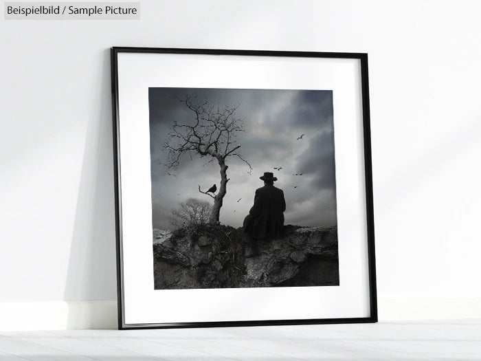 Framed artwork showing a person in a hat by a barren tree against a cloudy sky, displayed leaning on a white wall.