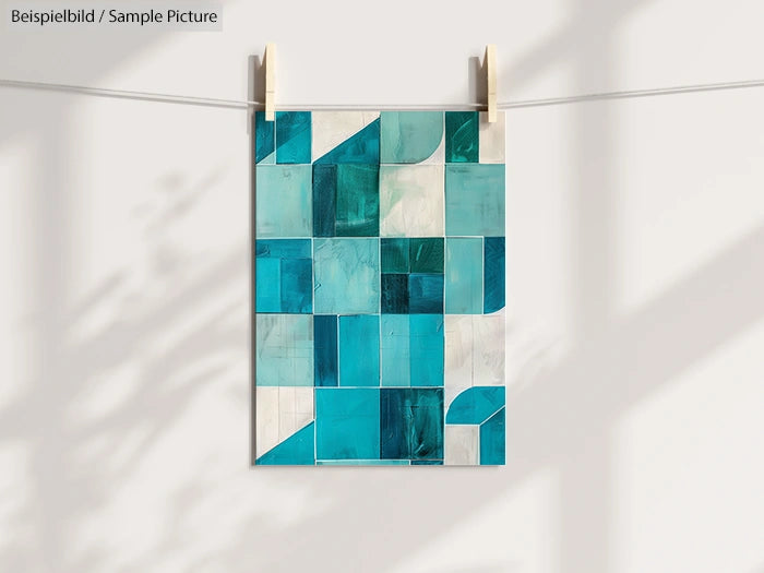 Teal and white geometric artwork hanging on a string with clothespins, soft light and shadow on background.