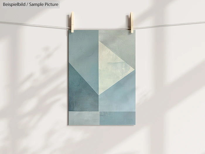 Abstract geometric painting with blue and gray tones, clipped to a line with shadows on a white wall.