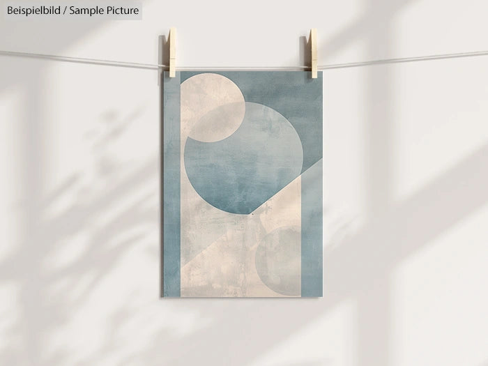 Minimalist abstract poster in blue and cream tones, hanging from a string against a white wall with shadows.