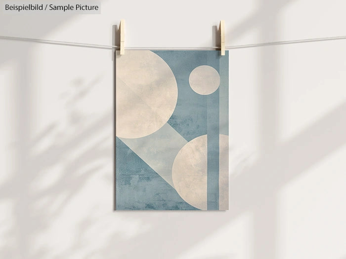 Minimalist geometric art print with circles and rectangles in blue and white, hanging on a line with clothespins.