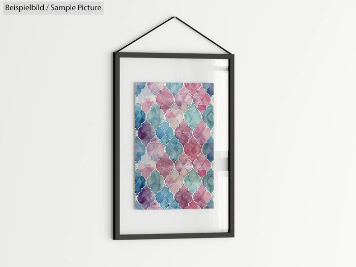 Framed watercolor painting with geometric patterns in pink, blue, and green hues, hanging on a white wall.