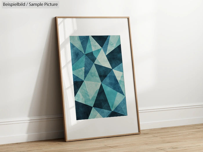 Framed geometric artwork with blue and teal triangles, leaning against a white wall on a wooden floor.