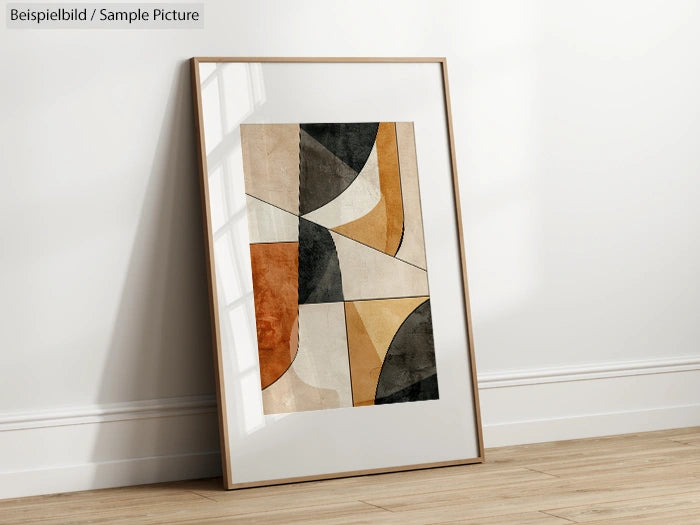 Framed abstract geometric art print with earth tones propped against a white wall on a wooden floor.