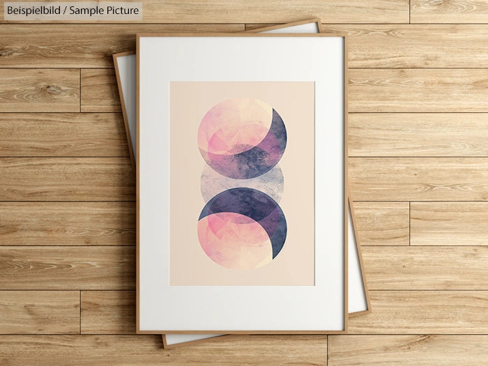 Framed abstract artwork with overlapping pink and blue circular shapes on a wooden floor background.