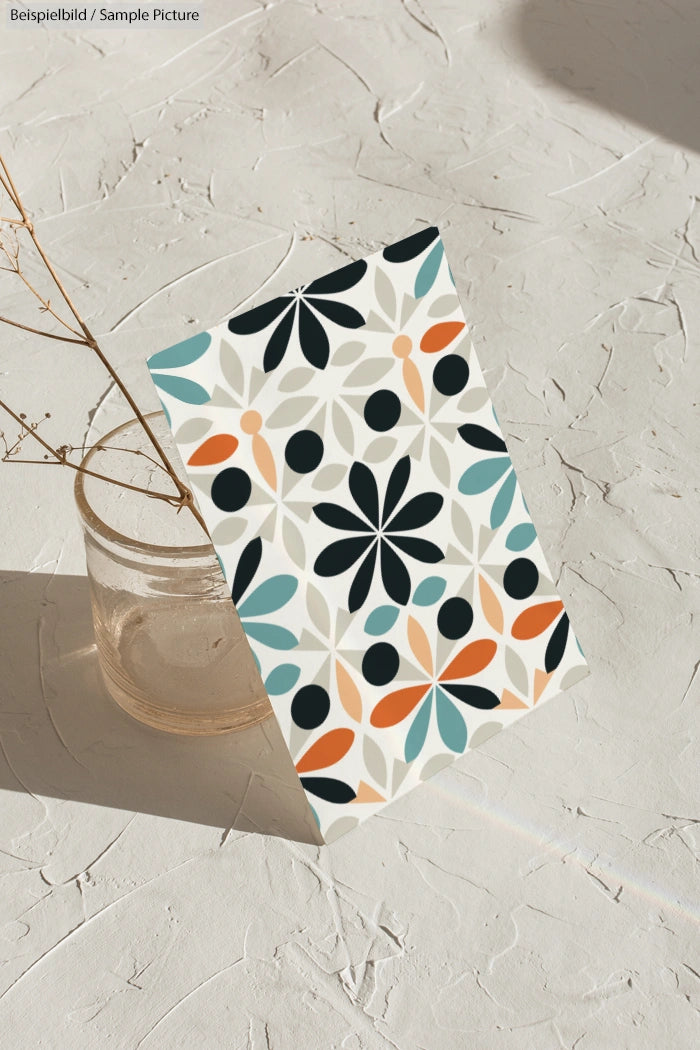 Colorful floral pattern card propped against glass on textured surface.