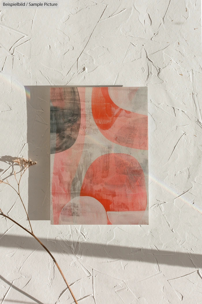 Abstract art with red and gray shapes on textured white paper, sunlight casting a rainbow reflection.