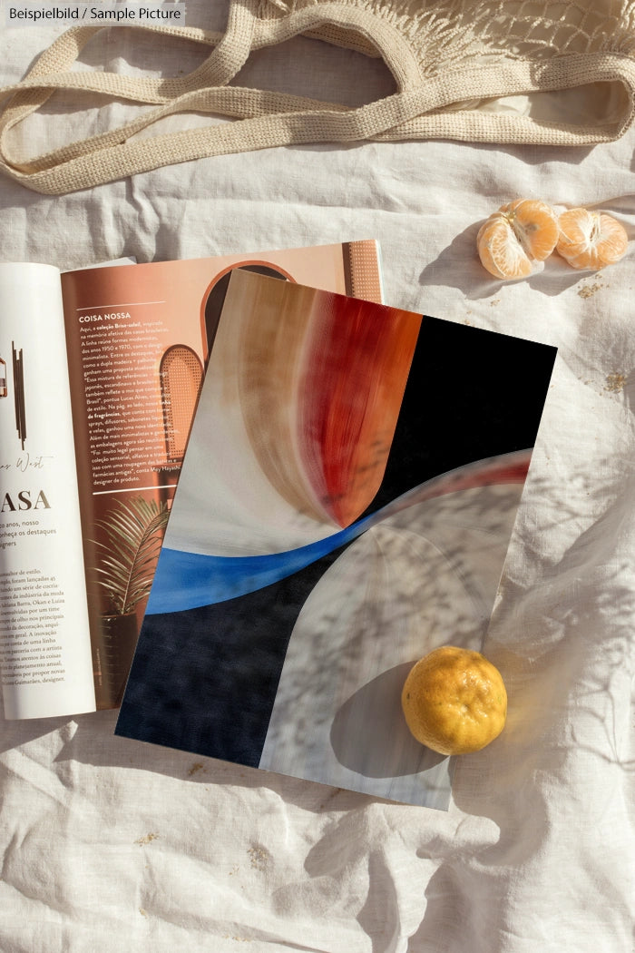 Abstract art print on linen with magazine, oranges, and woven bag on a sunlit table.