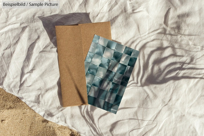 Abstract card with blue-green mosaic pattern on paper bag, resting on a cloth surface outdoors.