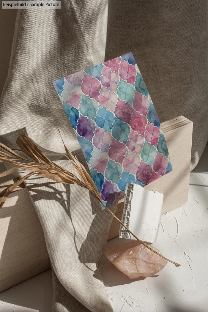 Geometric watercolor art with pastel hues of pink, blue, and green, displayed with natural textures and dried grass.