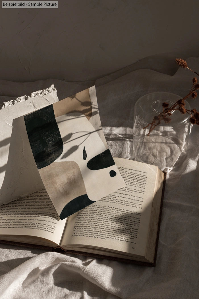 Open book with abstract black and white artwork on textured paper, dried leaves, and soft lighting.