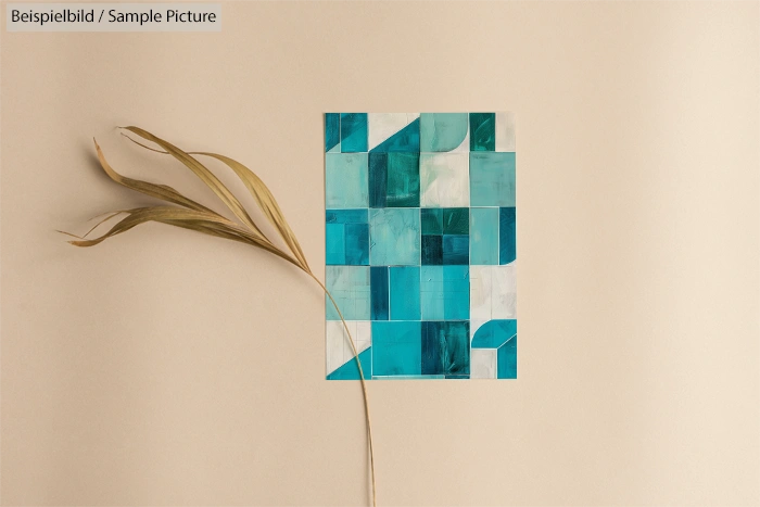 Modular art design with teal geometric shapes on beige background, next to a dried leaf.