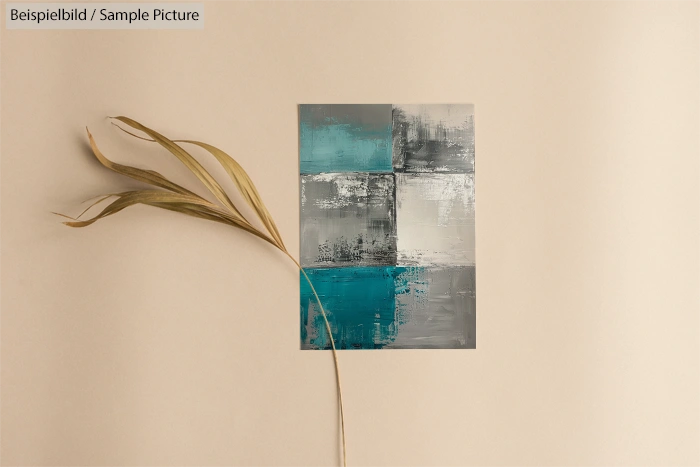 Abstract painting with teal and gray blocks on beige background next to dried plant stem.