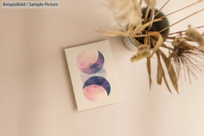 Abstract pastel art print with geometric shapes, next to a vase with dried flowers on a light surface.