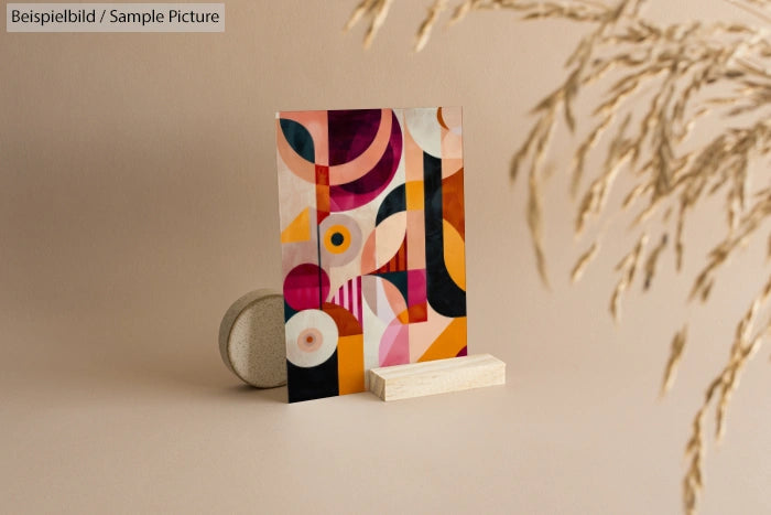 Abstract geometric artwork with colorful circles and shapes, displayed on a wooden stand, set against a neutral backdrop.