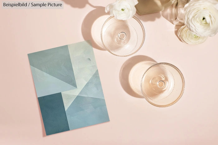 Geometric teal artwork on table with round glasses and white flowers in vase.