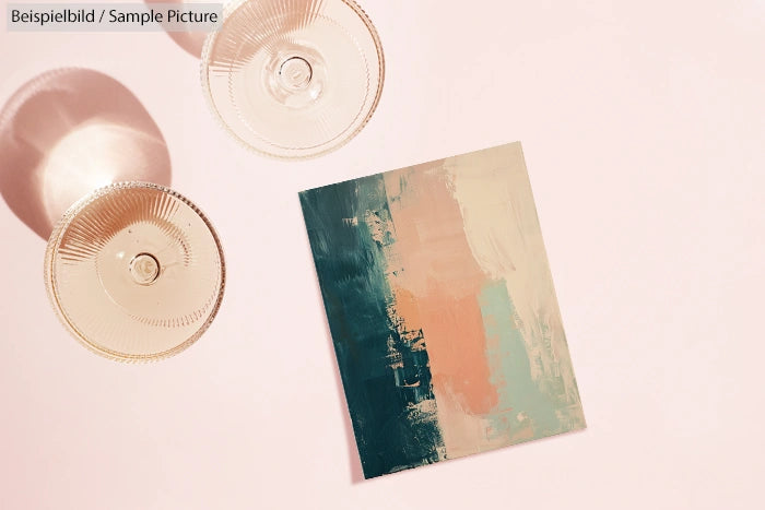 Abstract painting with teal, pink, and beige hues on a light surface, accompanied by two transparent textured glasses.