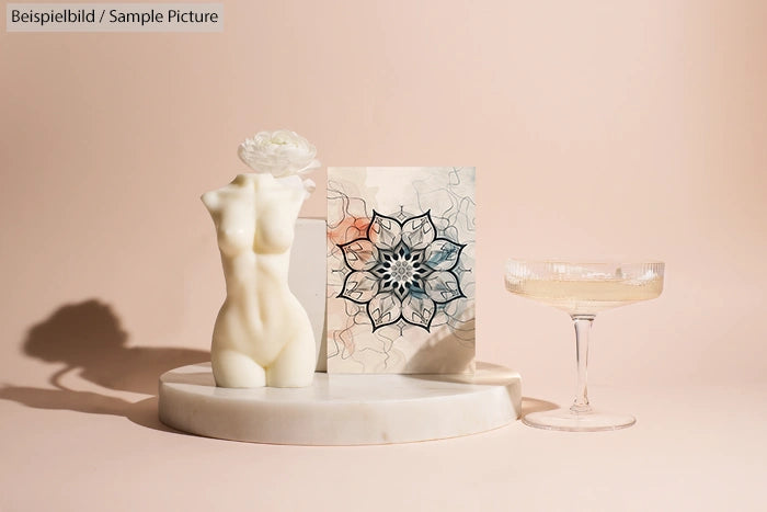 Artistic display of a female torso sculpture, mandala artwork, and a champagne glass on a marble platform.