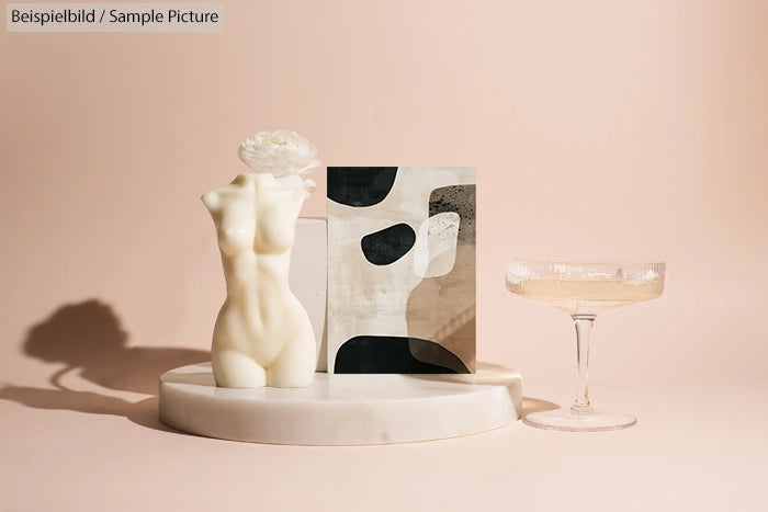 Sculpted torso candle, abstract art, and a glass on marble tray against beige background.