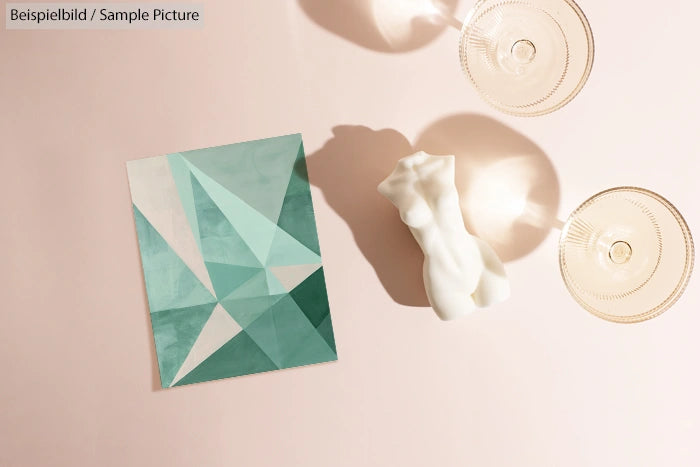 Geometric abstract art on teal paper, beside a white ceramic torso sculpture and two champagne glasses.