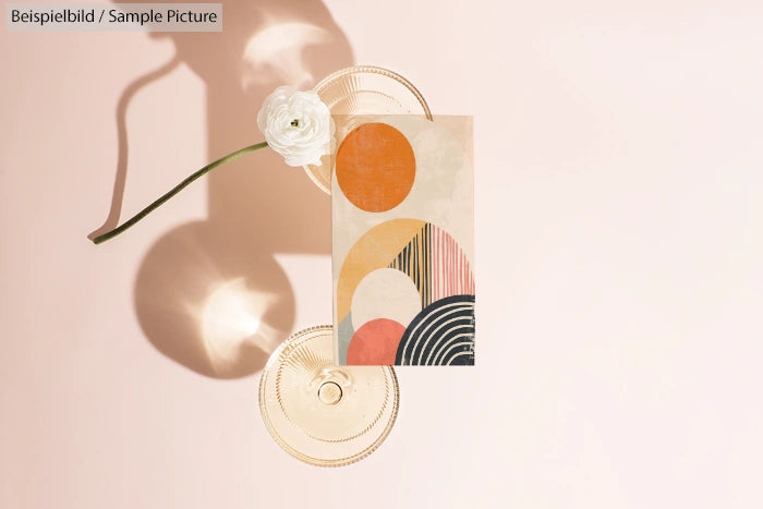 Geometric artwork with circles and arches on light background, next to a single white flower.