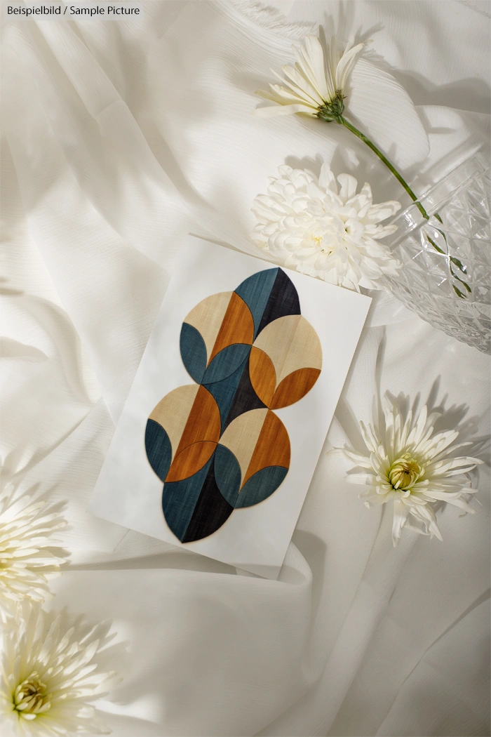 Geometric art print on white fabric, surrounded by white flowers and a crystal vase.