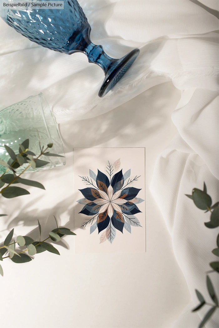 Decorative card with floral design on white fabric, surrounded by eucalyptus leaves and blue glass vases.