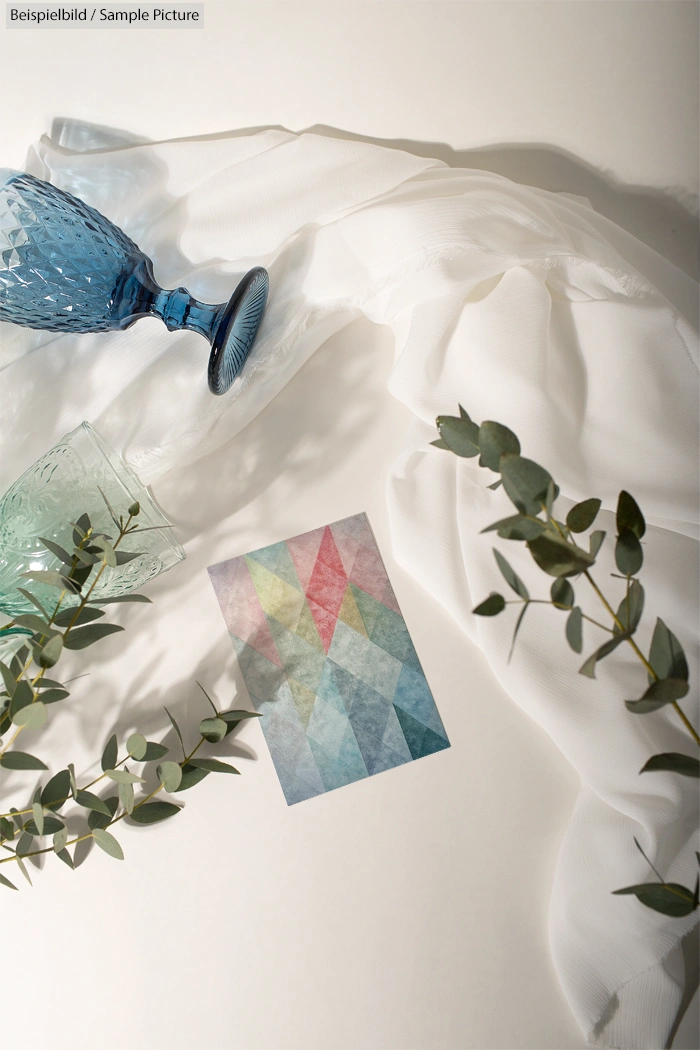 Colorful geometric card with leaves, blue glass, and white cloth on a white background.