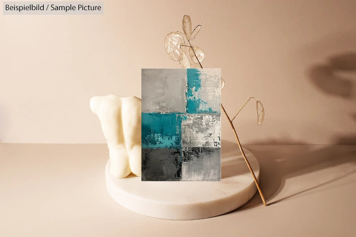 Abstract painting with teal, gray blocks on a cream pedestal with a delicate dried plant in a minimalist setting.