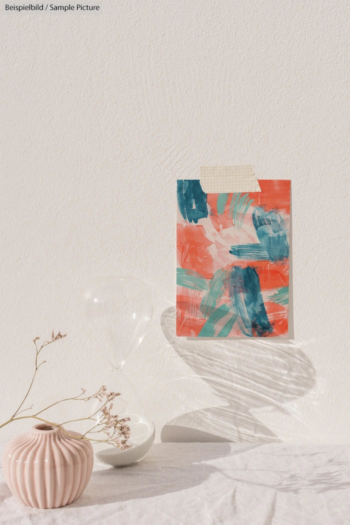 Abstract painting with teal and coral brushstrokes on a wall, minimal vase with dried flowers and hourglass nearby.