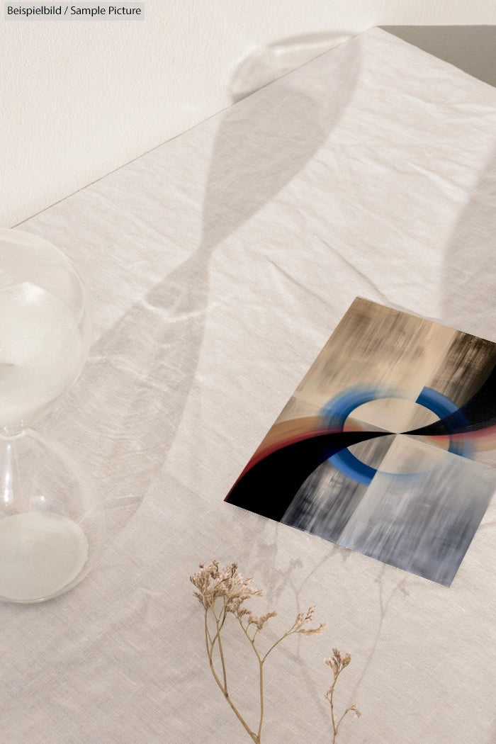 Abstract art print with blue and red circles on table next to hourglass and dried flowers.