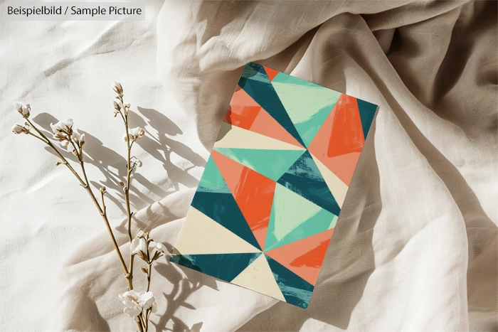 Abstract geometric pattern in teal, orange, and cream on fabric backdrop with dried flowers.