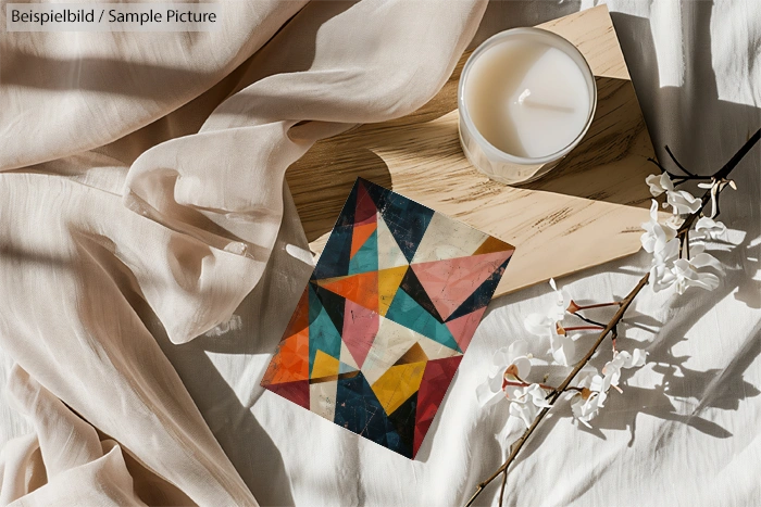 Geometric abstract card on wooden board with candle and decorative flowers on beige fabric.