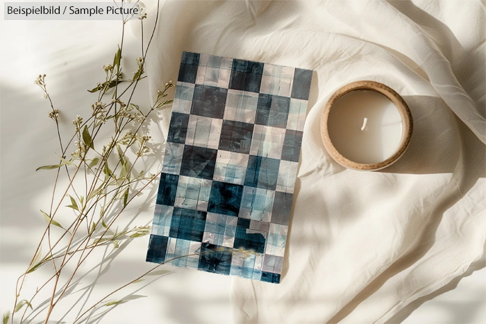 Patterned card on white fabric with candle and dried herbs.