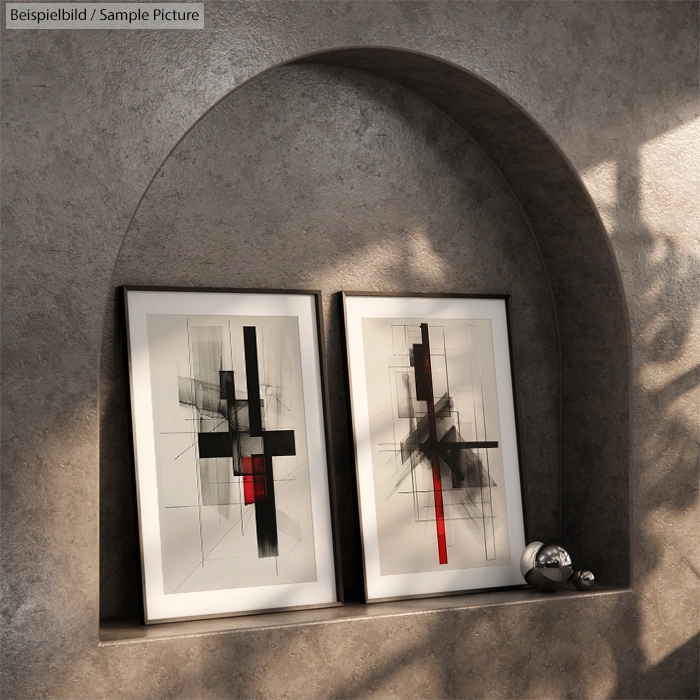 Two framed abstract artworks with black and red geometric patterns on a shelf in a softly lit alcove.